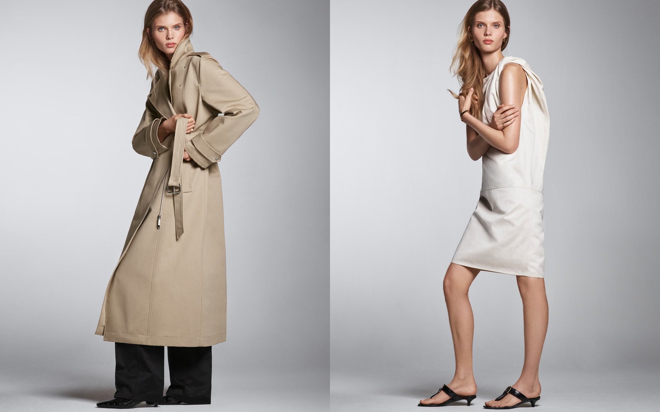 Two fashion models pose in a studio with neutral background. One wears a trench coat and the other wears a white dress and black sandals.