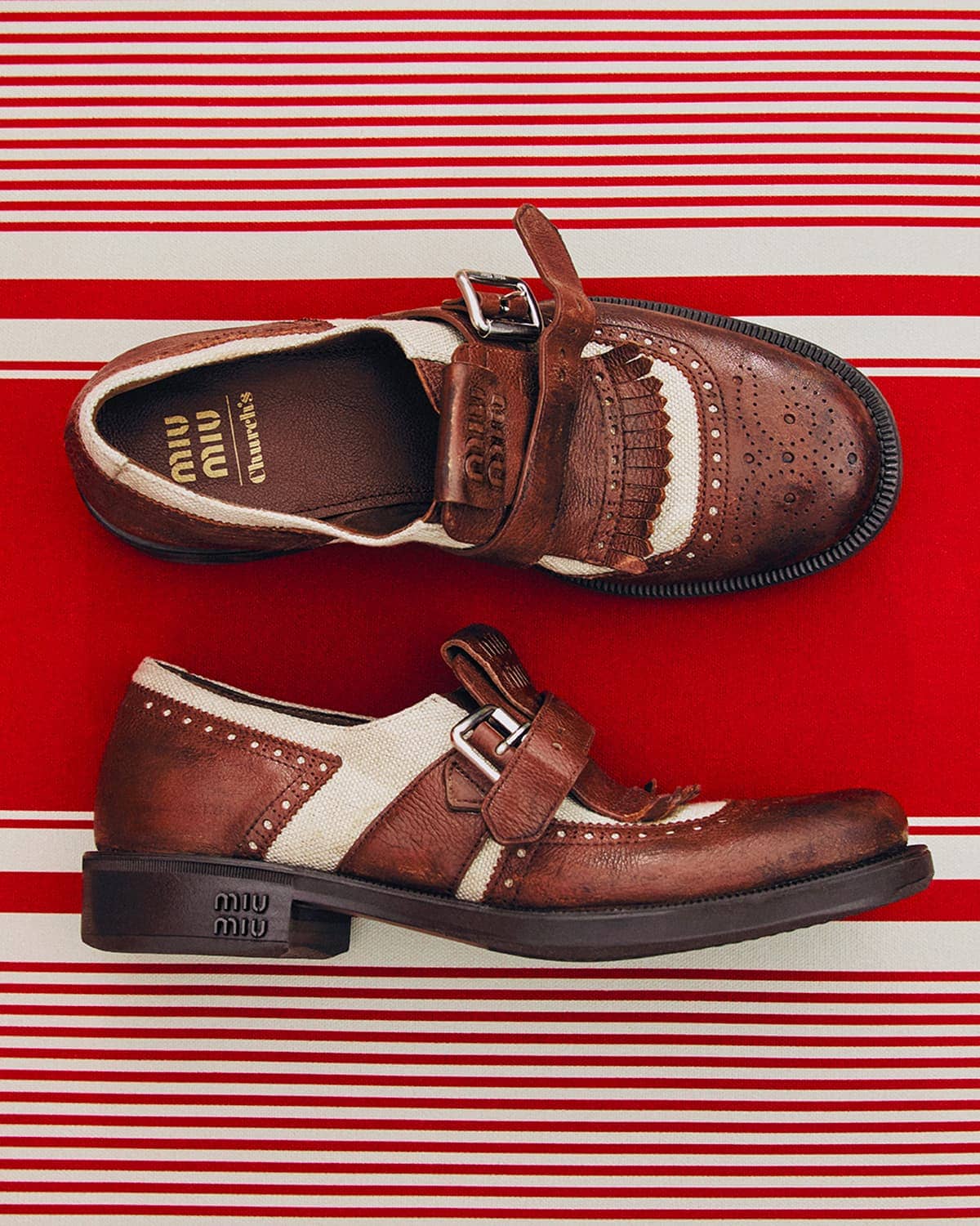 A pair of brown leather Miu Miu Church's shoes with a buckle strap on a red and white striped surface, displayed in a studio setting.