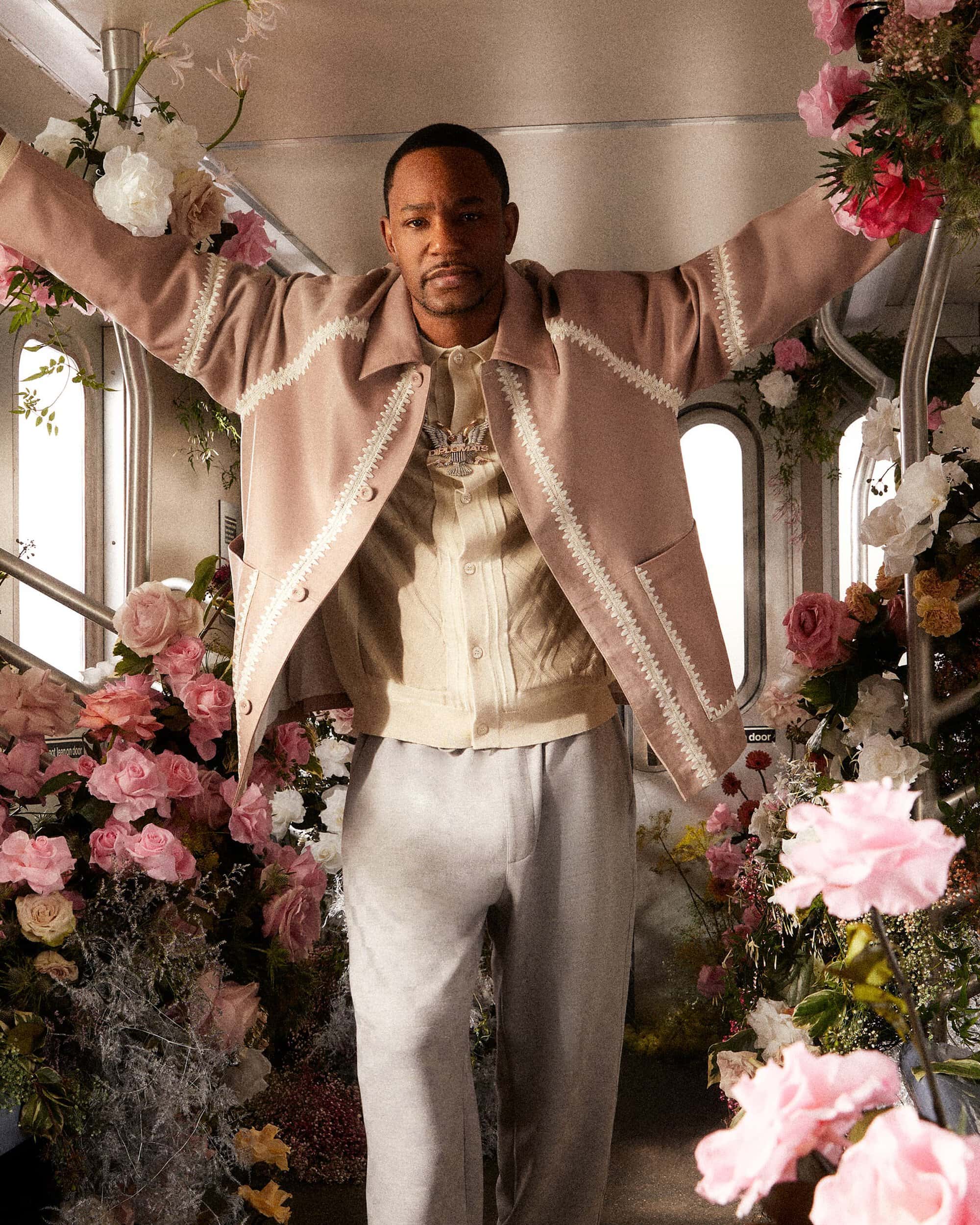Man in pink jacket surrounded by pink and white flowers in a subway car, looking at the camera with a neutral expression.