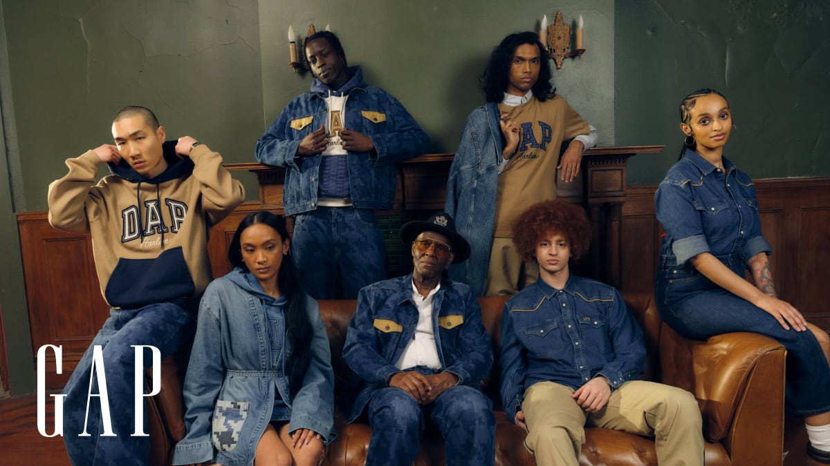 Diverse group of models wearing Gap clothing are seated indoors in a studio setting, showcasing a variety of denim and casual wear.