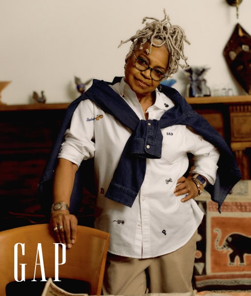 Portrait of an African-American woman with glasses and dreadlocks wearing a button-down shirt and a denim jacket tied around her shoulders.