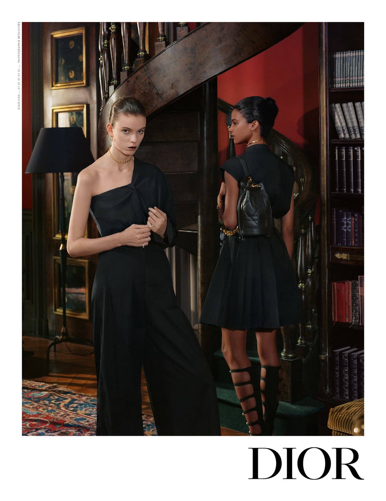 Two fashion models wearing elegant black dresses pose in an interior with a staircase and bookshelves, showcasing a luxury fashion brand.
