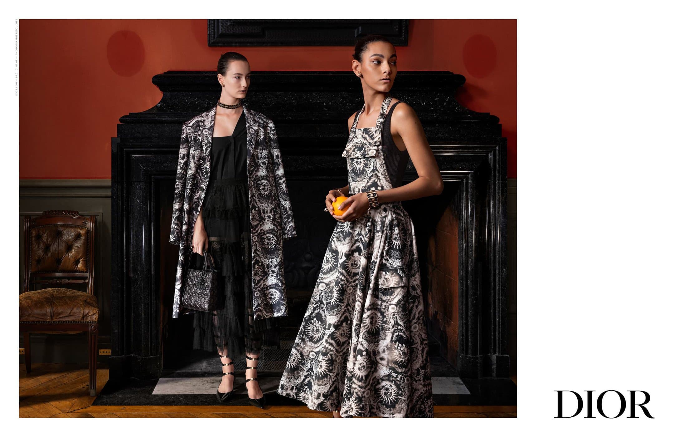 Two female models in patterned monochrome outfits posing in front of a dark stone fireplace with red walls.