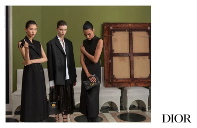 Three female models in black attire posing in a green walled room with a large wooden framed artwork for Dior.