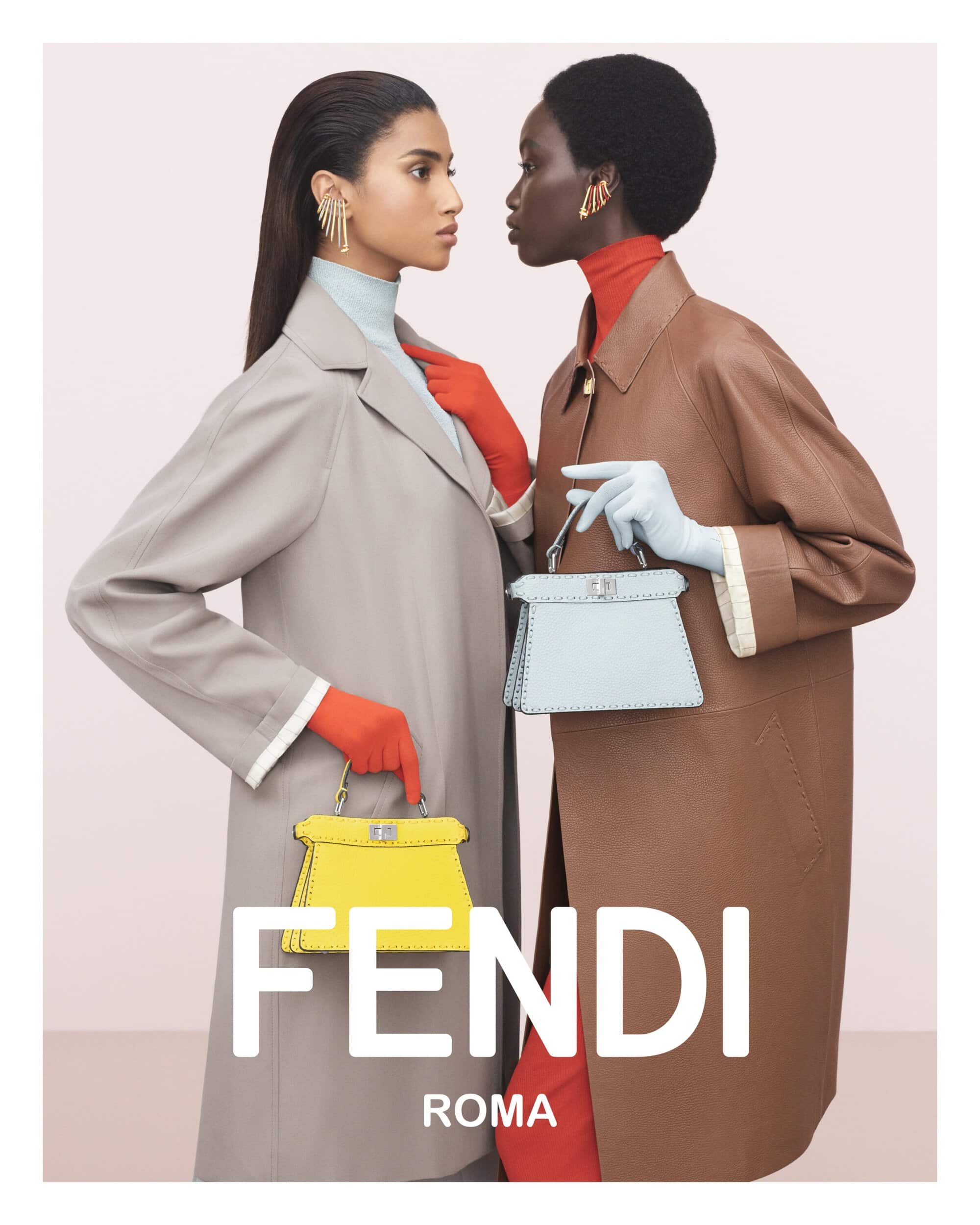 Two fashion models in coats holding Fendi handbags with a pink gradient background, shot in a studio with natural lighting.