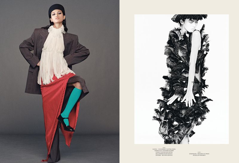 Editorial fashion shot of an adult woman in a gray oversized blazer, flowing blouse, skirt, teal socks, and black hat posing in a photo studio.