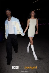 A man in a blue and yellow jacket and a woman in a pale yellow dress walking together at night