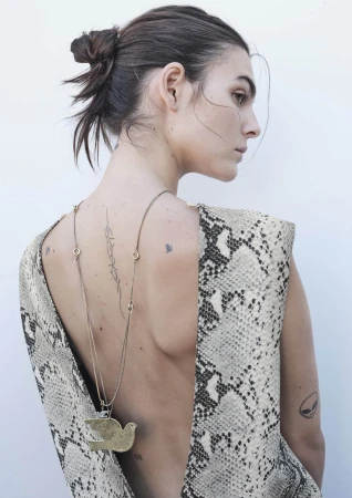 Woman with messy bun wears snake-print low-back dress and pendant necklace, showcasing back tattoos in a minimalist studio setting.