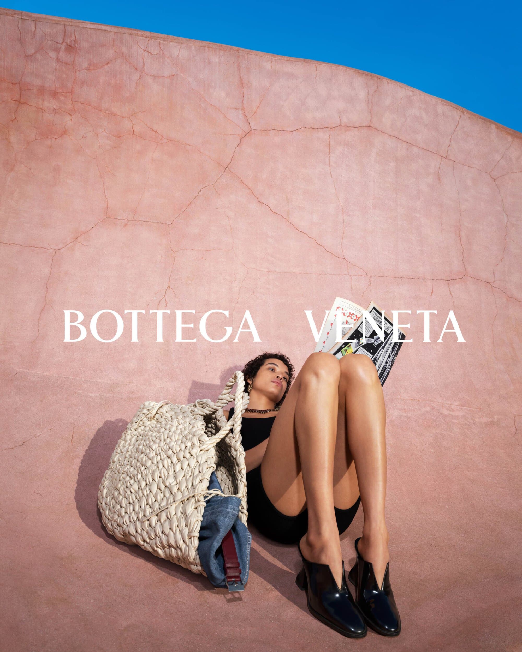 Elegant ad featuring a woman lounging with a magazine, showcasing a Bottega Veneta bag and sleek black mules on a sun-drenched backdrop.