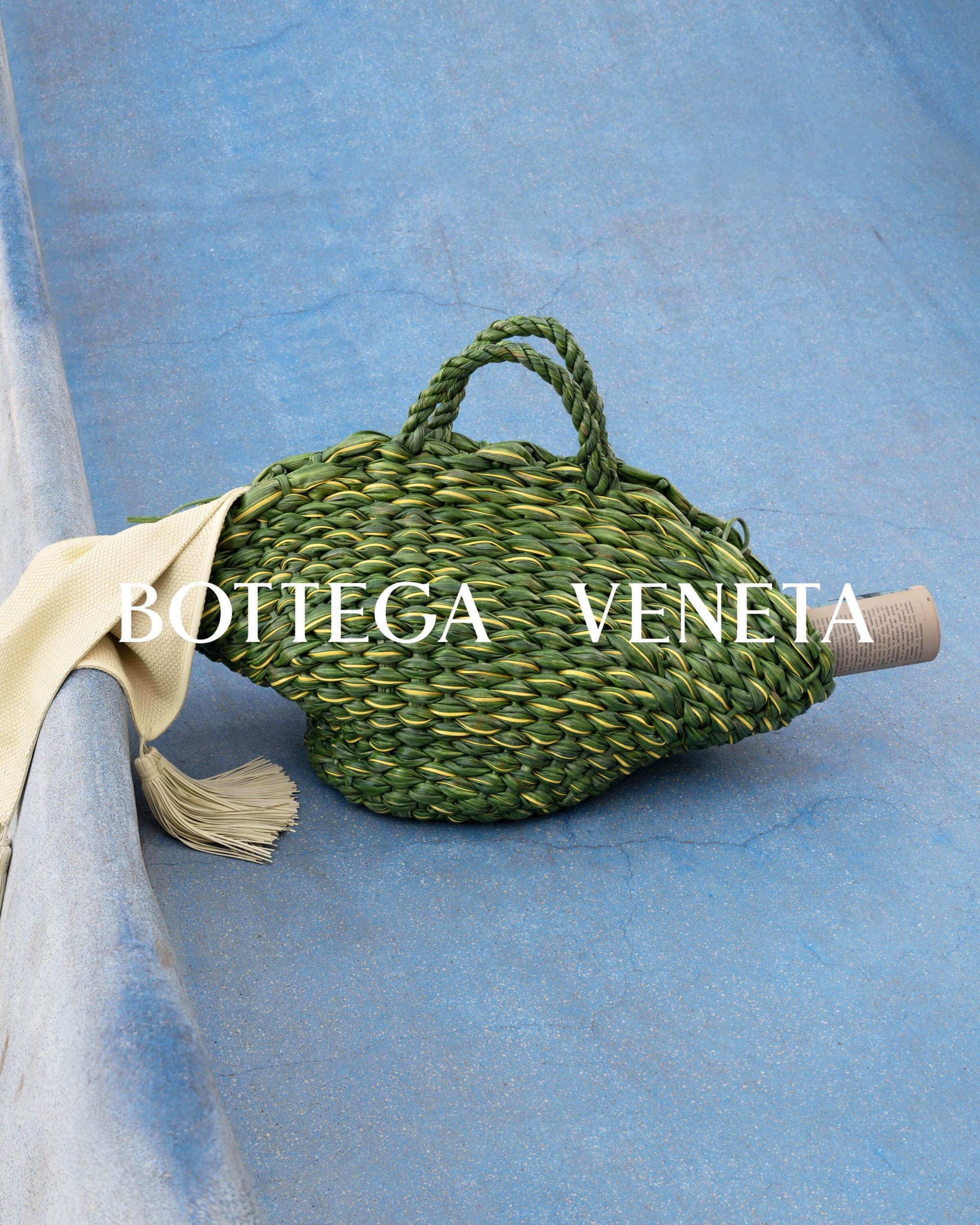Woven green handbag with rope handles, paired with a soft beige scarf, set against a light blue textured background, studio lighting.