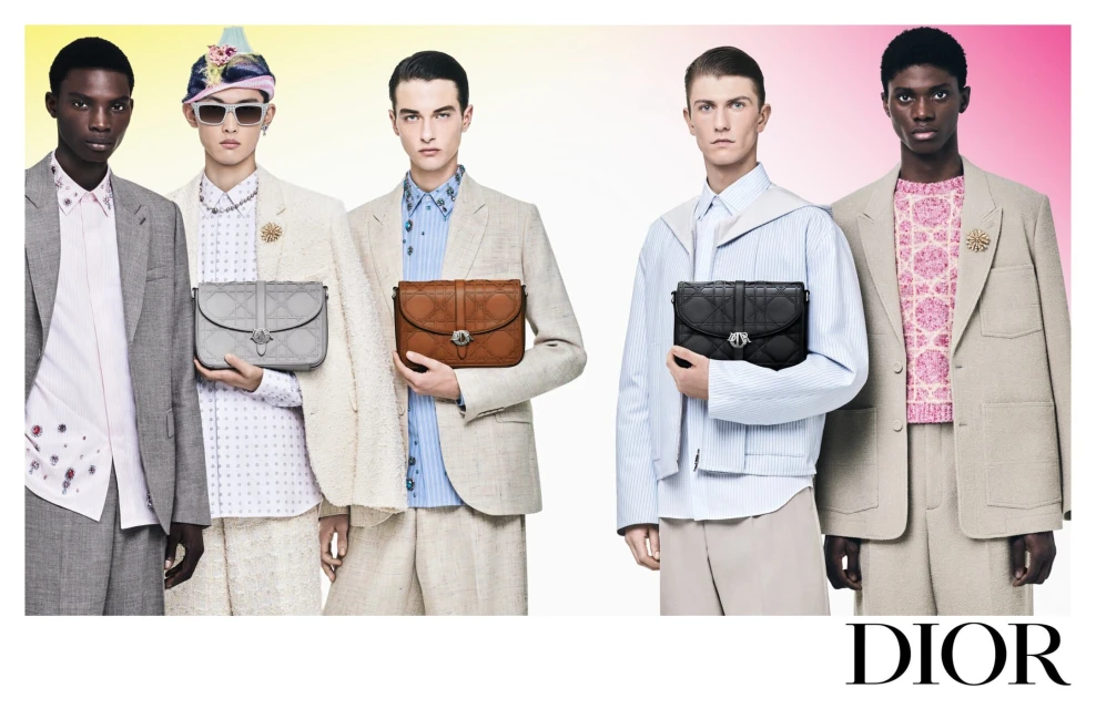 Five diverse male fashion models pose against a gradient backdrop, showcasing a collection of handbags and stylish blazers. Dior logo is present.