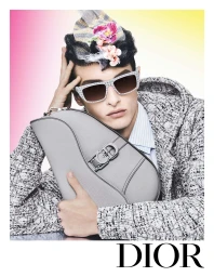 Model wearing a patterned hat with floral accents, sunglasses, and a grey handbag for Dior Men's Spring 2024 campaign.