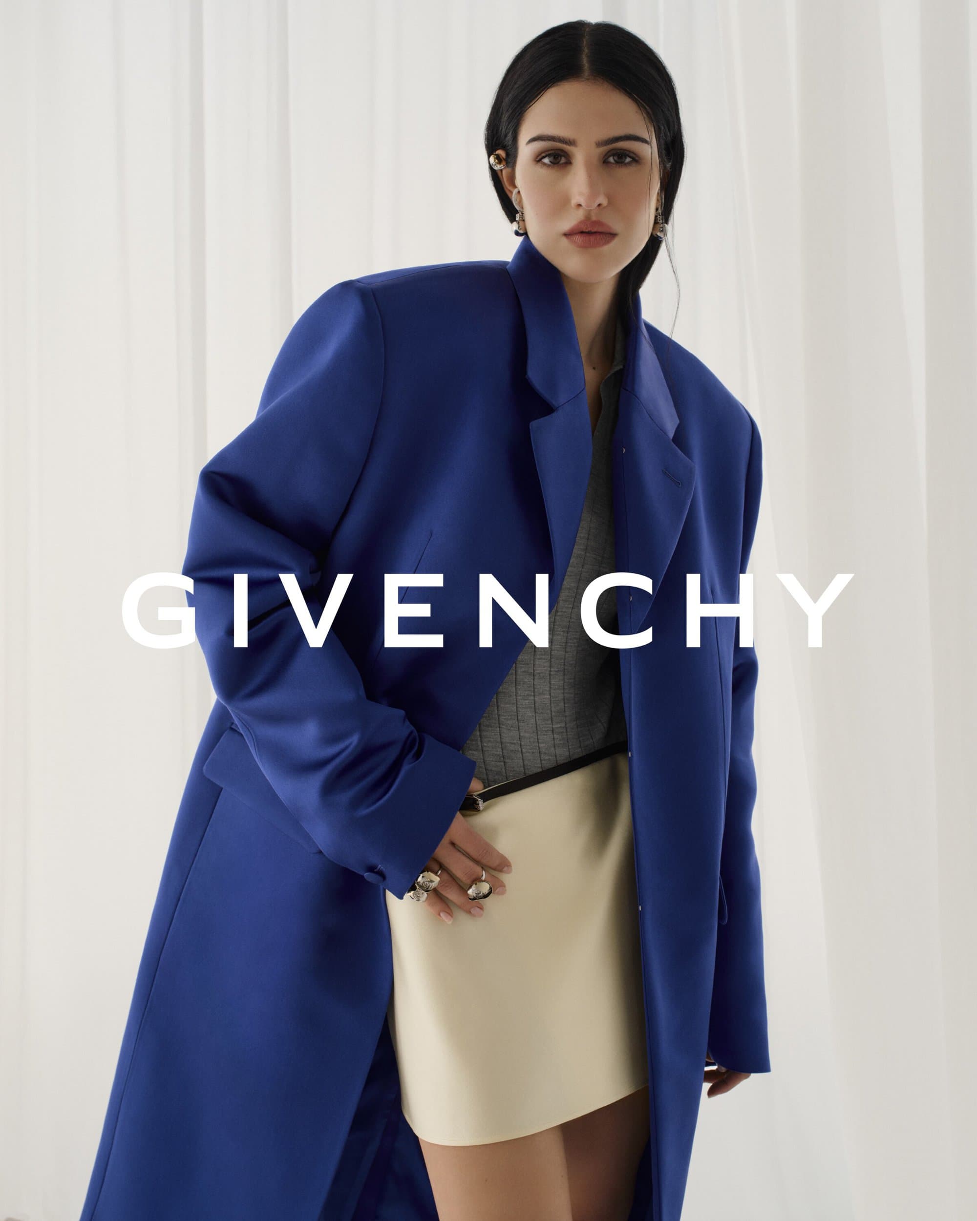 Fashion editorial shot of a woman in a cobalt blue blazer and cream-colored skirt, posing against a light backdrop with the GIVENCHY logo.