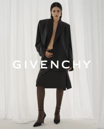 Model Amelia Gray in an oversized black blazer and matching skirt against white curtain background for Givenchy