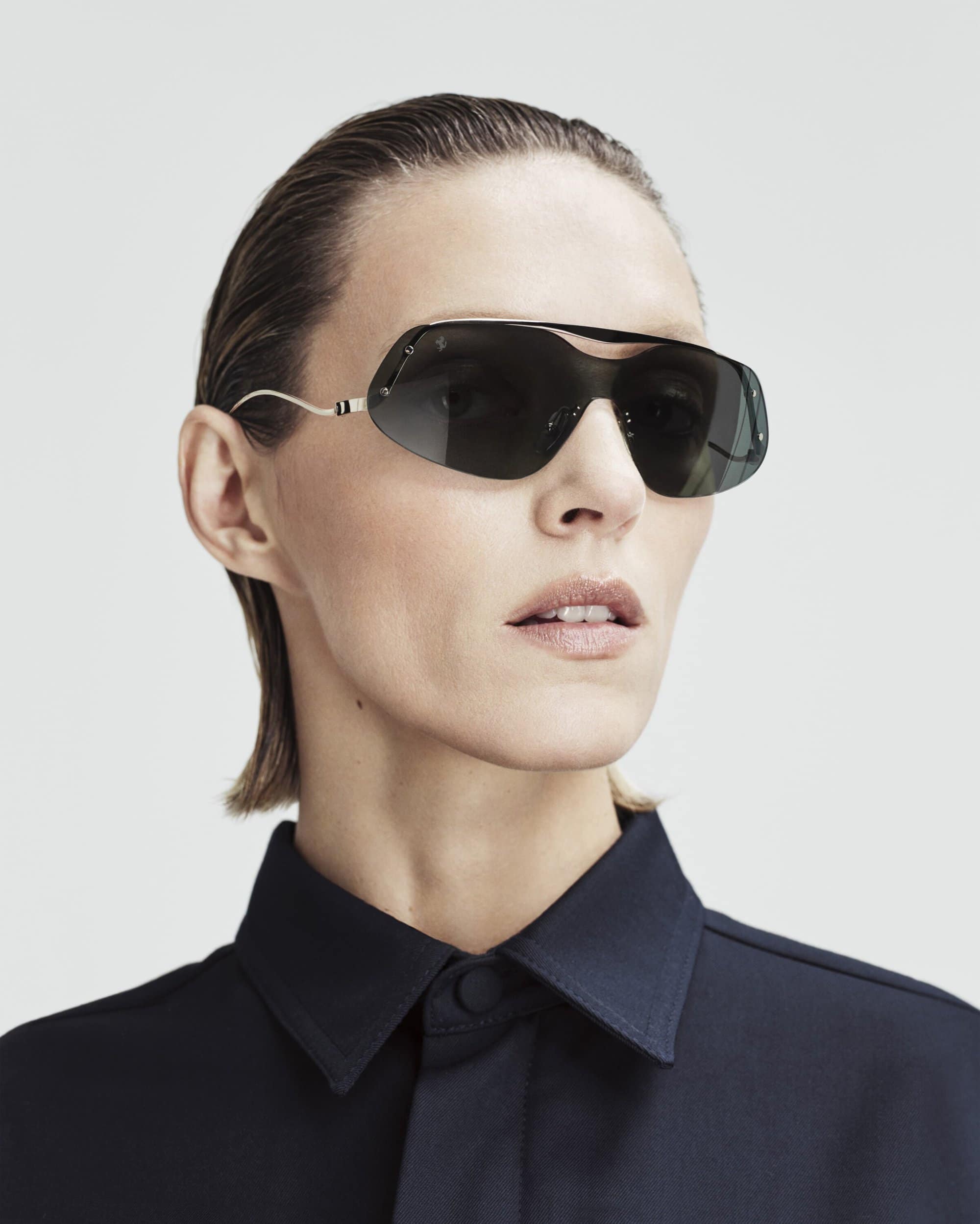 Headshot of adult female model wearing aviator-style sunglasses and a navy button-down shirt in a brightly lit, neutral studio.