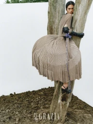 Model wearing a striped dress and black leather gloves embracing a tree trunk against a white background