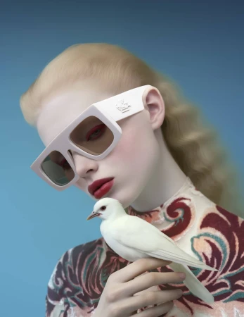 Fashion portrait of a blond woman with white sunglasses holding a white dove in a photo studio with a blue background.