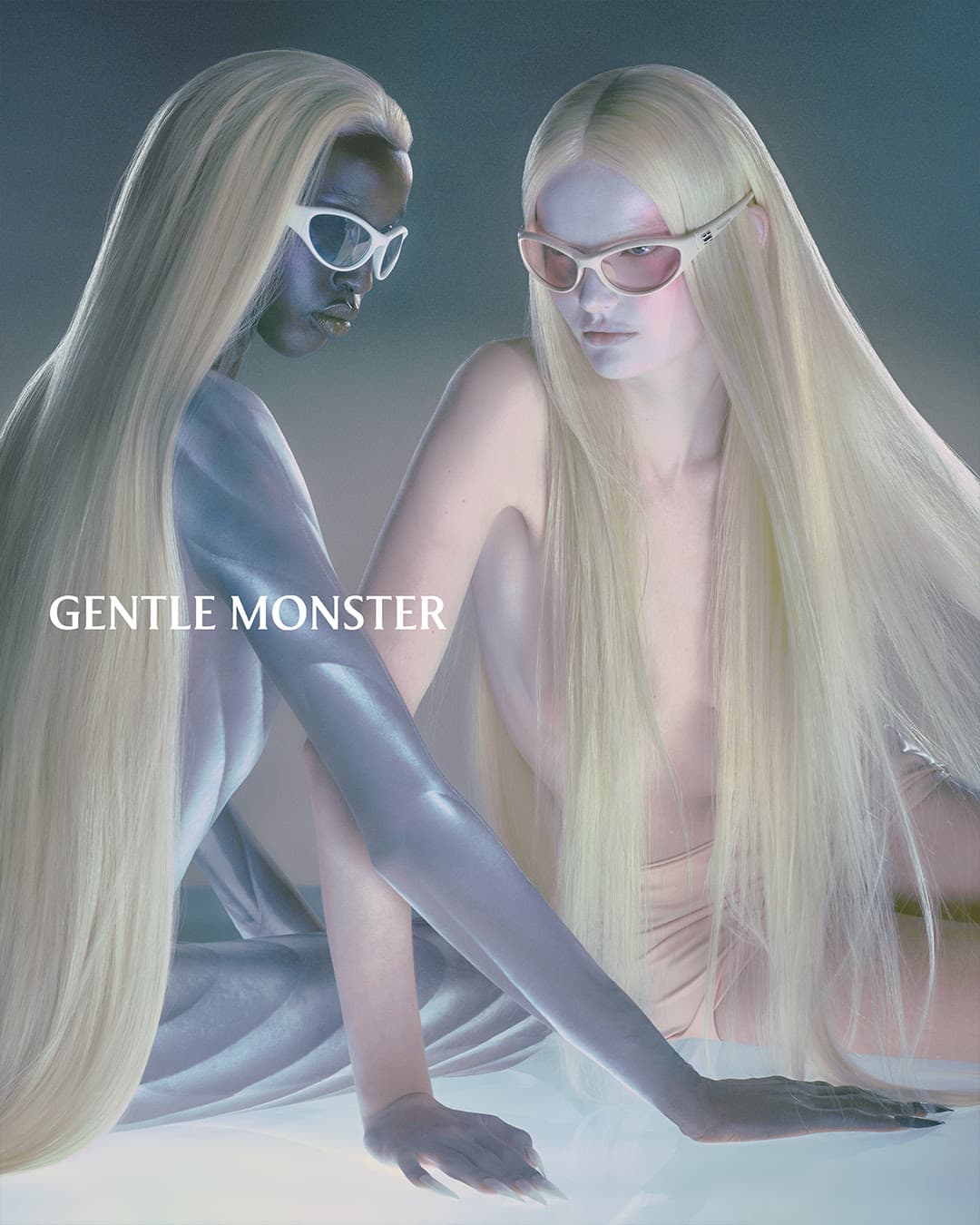 Two models pose indoors for a Gentle Monster eyewear advertisement. They wear glasses and have long, light blonde hair.