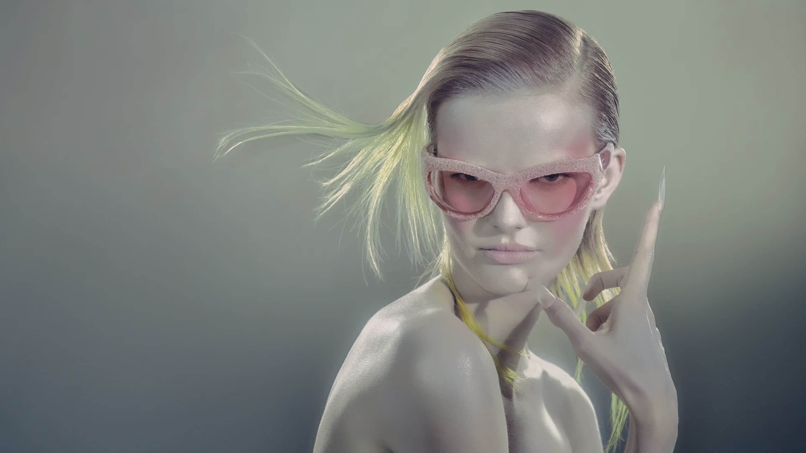 A fashion portrait features a model wearing pink sunglasses, showcasing light blonde hair with green accents against a soft grey background.