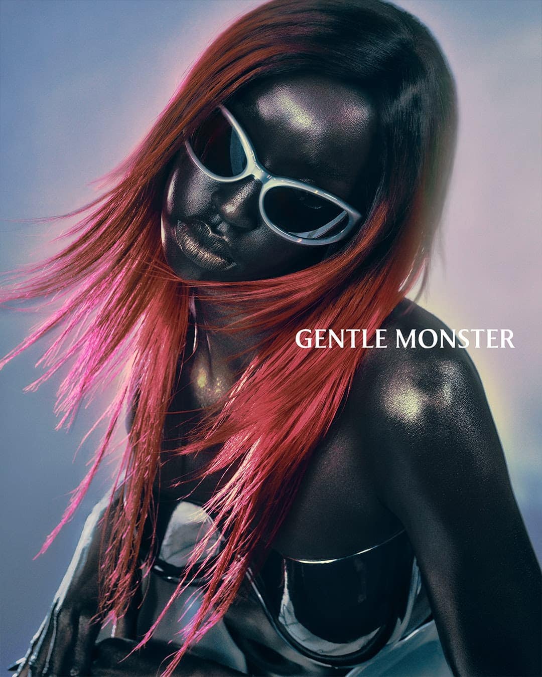 Dark-skinned model with pink-tipped red hair poses wearing white-framed sunglasses with a blue gradient background, and Gentle Monster logo.