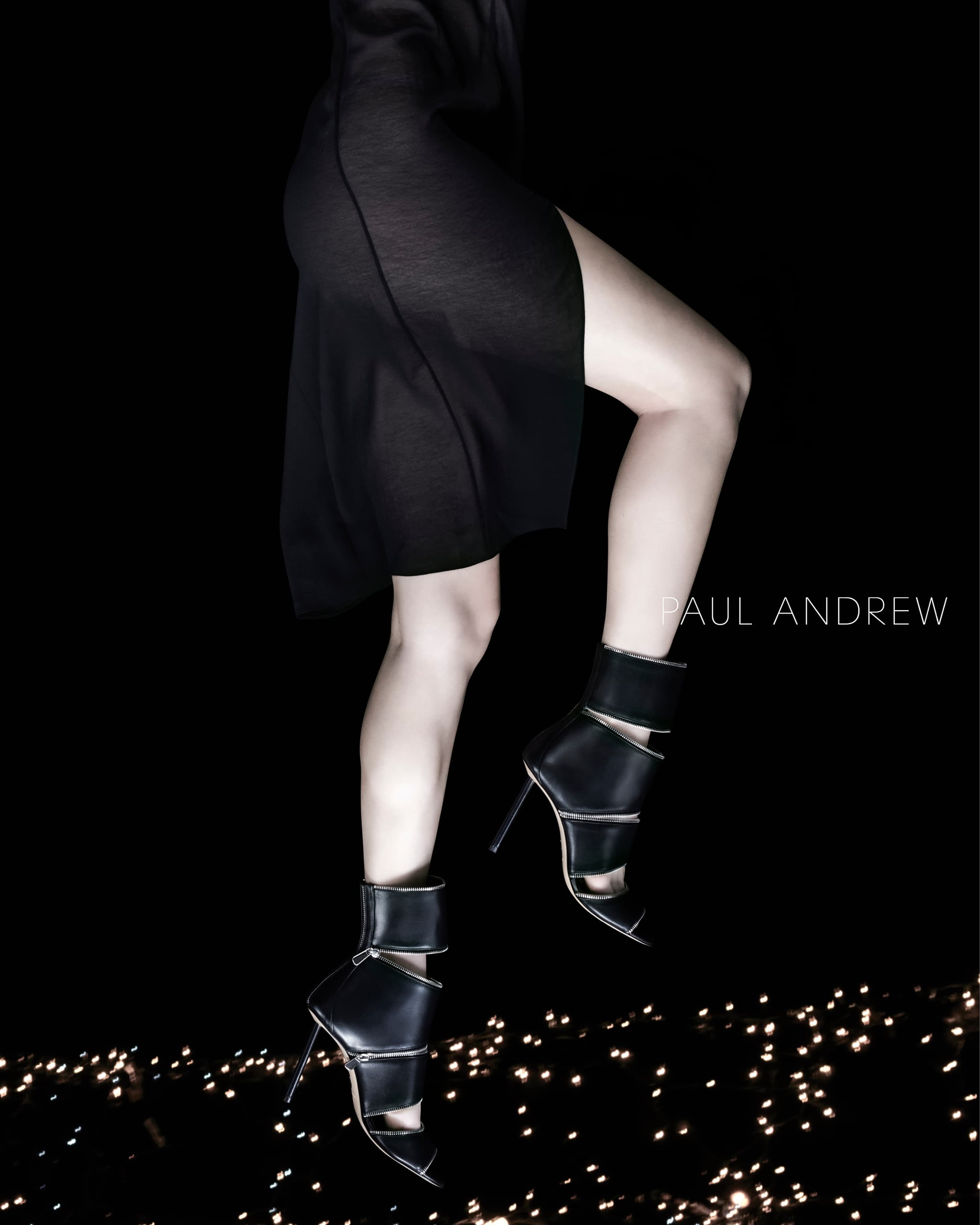 Fashion shot featuring a fair-skinned adult woman in a black dress and high heel shoes, posed against a black backdrop with bokeh lights.