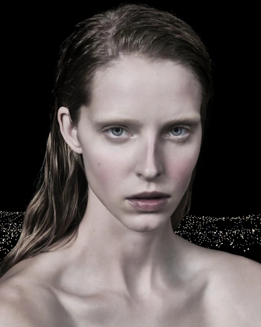 Close-up studio portrait of a young adult woman with light skin and wet hair against a dark background with abstract lights.