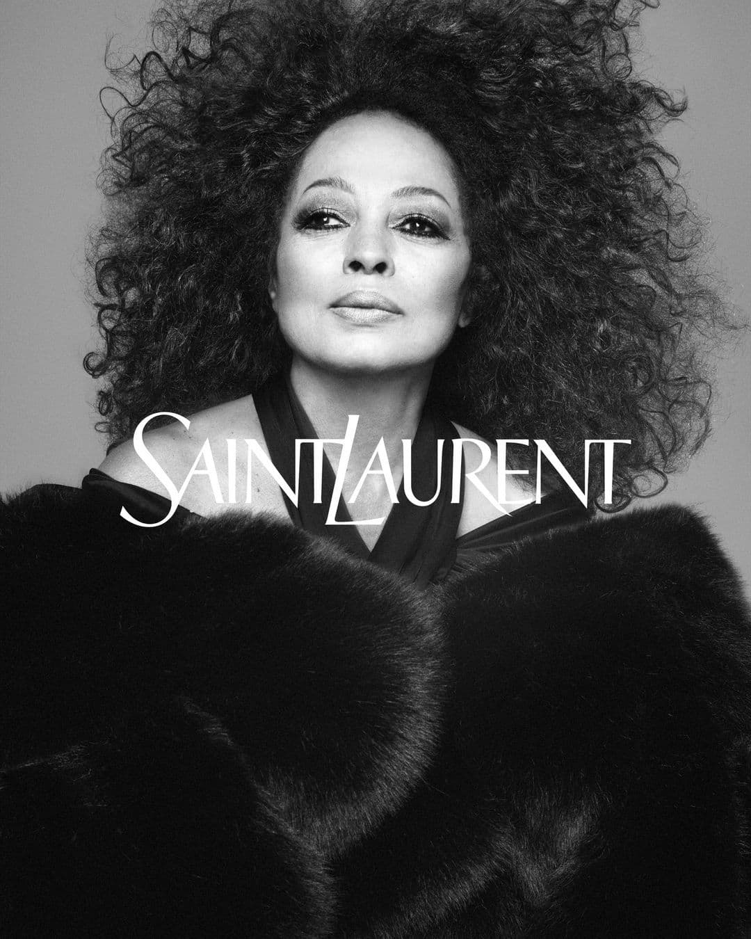 Black and white portrait of a mature African-American woman with large curly hair wearing a dark fur coat, with Saint Laurent logo.