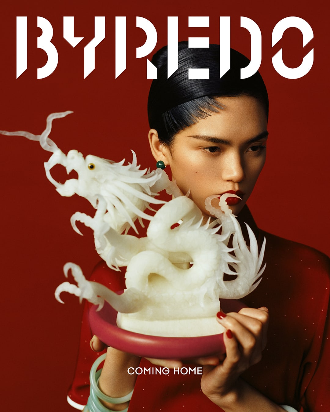 Elegant woman in red dress holds white dragon sculpture against a red background in a beauty campaign for Byredo.