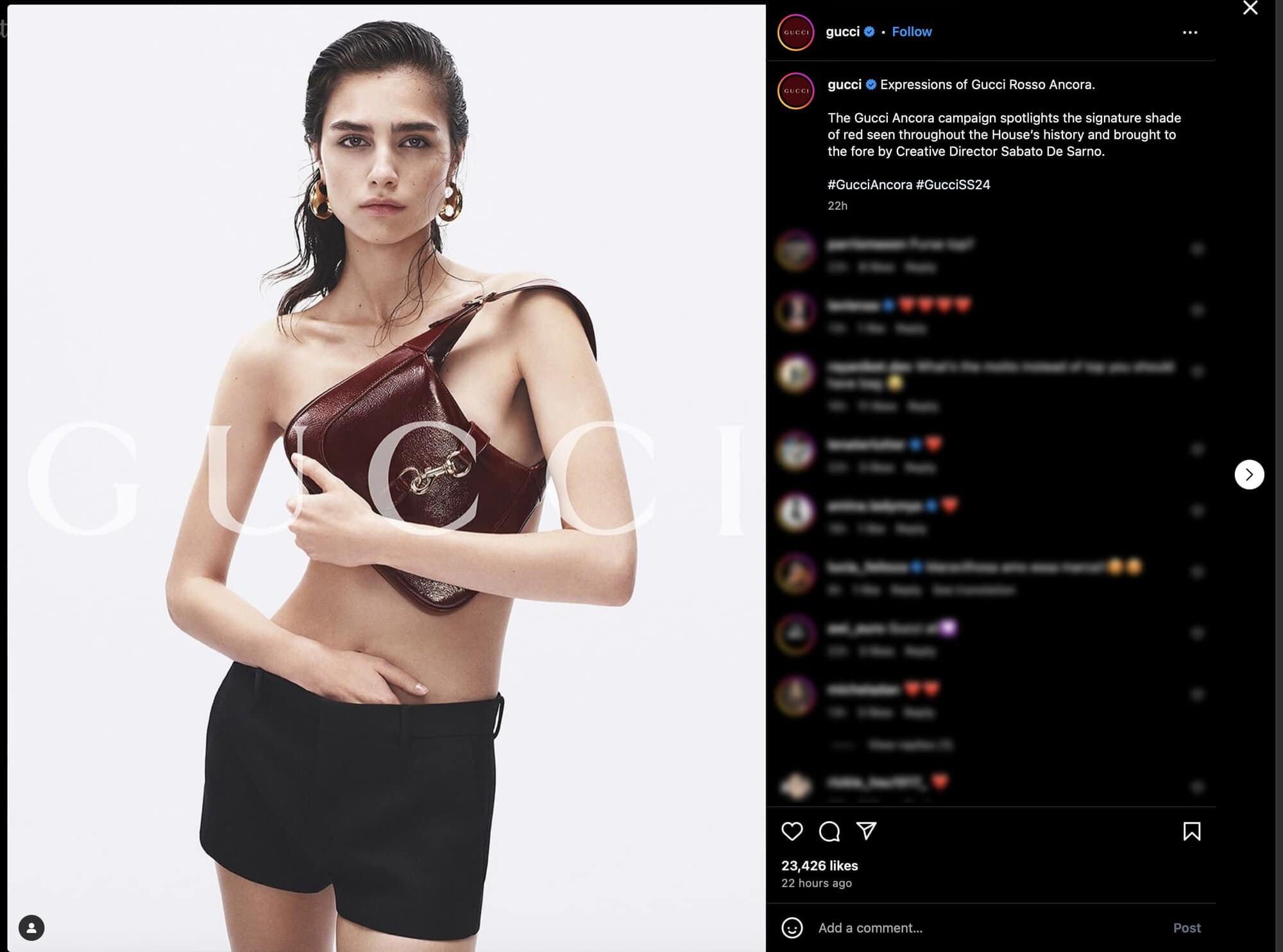A young woman poses in a fashion shot wearing black shorts and a red leather Gucci purse with a metal horsebit detail.