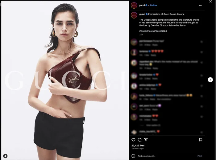 Model holding a dark red leather shoulder bag against a plain white background, wearing black shorts and round earrings