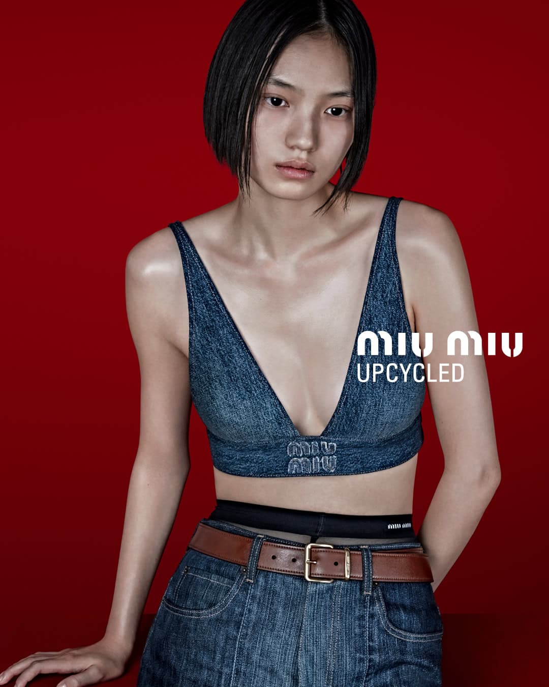 A woman poses in a denim top and jeans against a vibrant red backdrop, showcasing a minimalist yet fashionable style for a clothing brand.