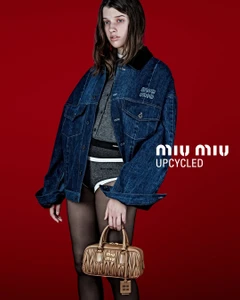 Model Ever Anderson wearing an oversized denim jacket and carrying a quilted brown handbag against a solid red studio background