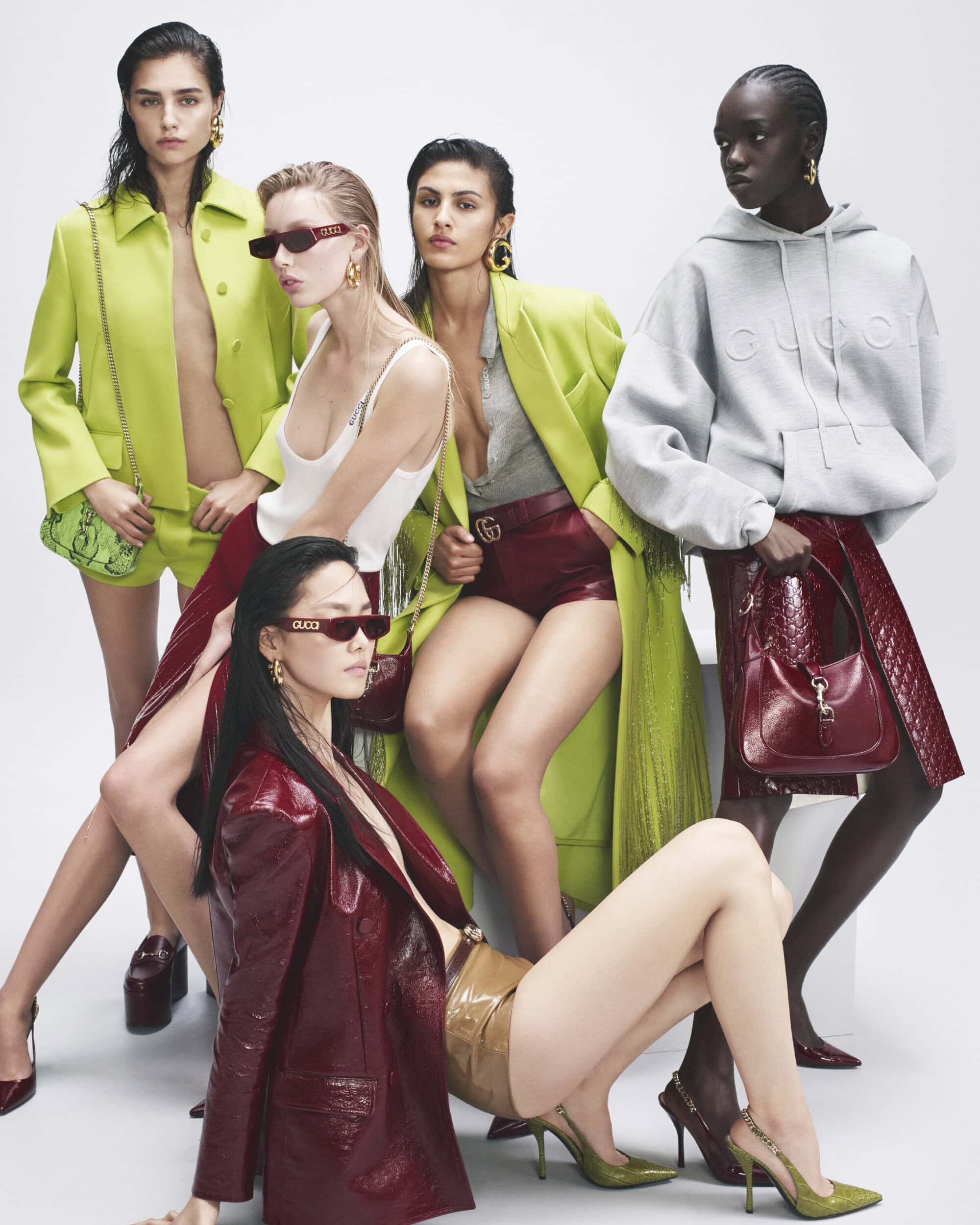 Group fashion shot of five diverse models in designer clothing and sunglasses posing in a studio with a white backdrop for a studio shot.