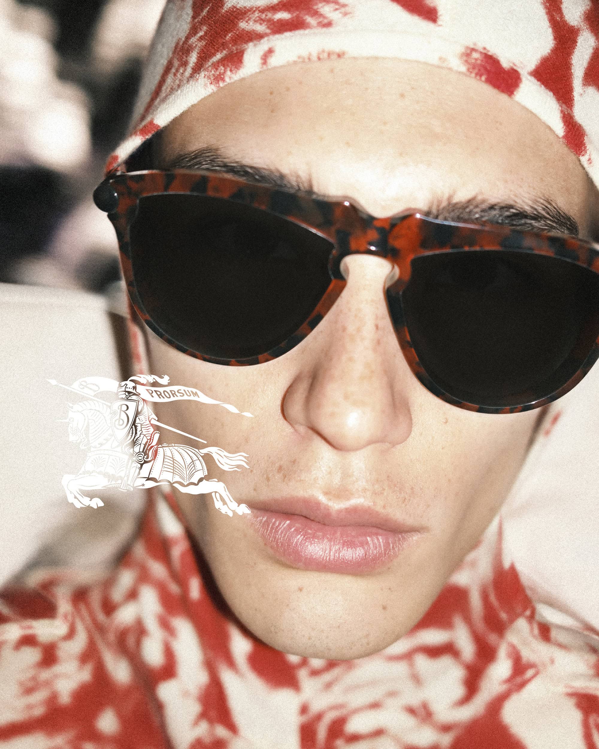 Close-up portrait of an adult male wearing sunglasses and a patterned shirt and head covering, with a Burberry logo illustration.