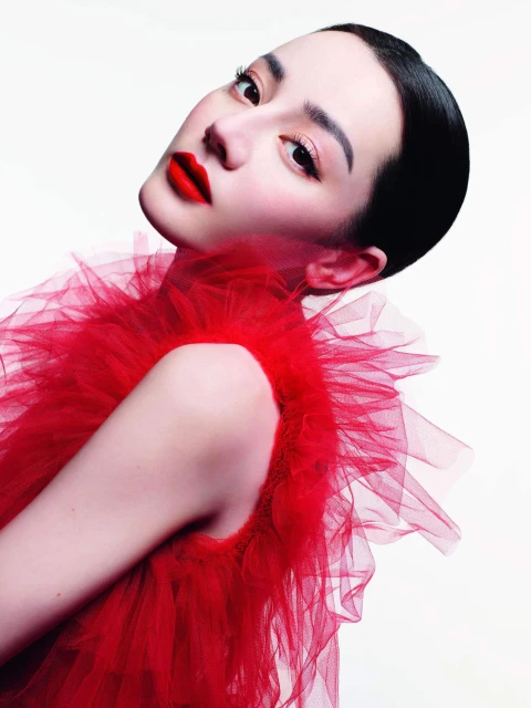 Portrait of an Asian woman with red lipstick and a red ruffled dress against a white backdrop. She is angled slightly towards the camera.