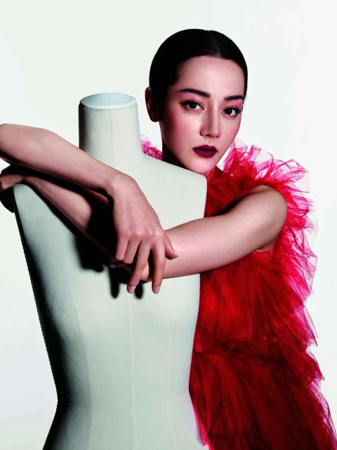 Glamorous woman in a red tulle dress poses elegantly with a mannequin in a bright studio, showcasing fashion and beauty.