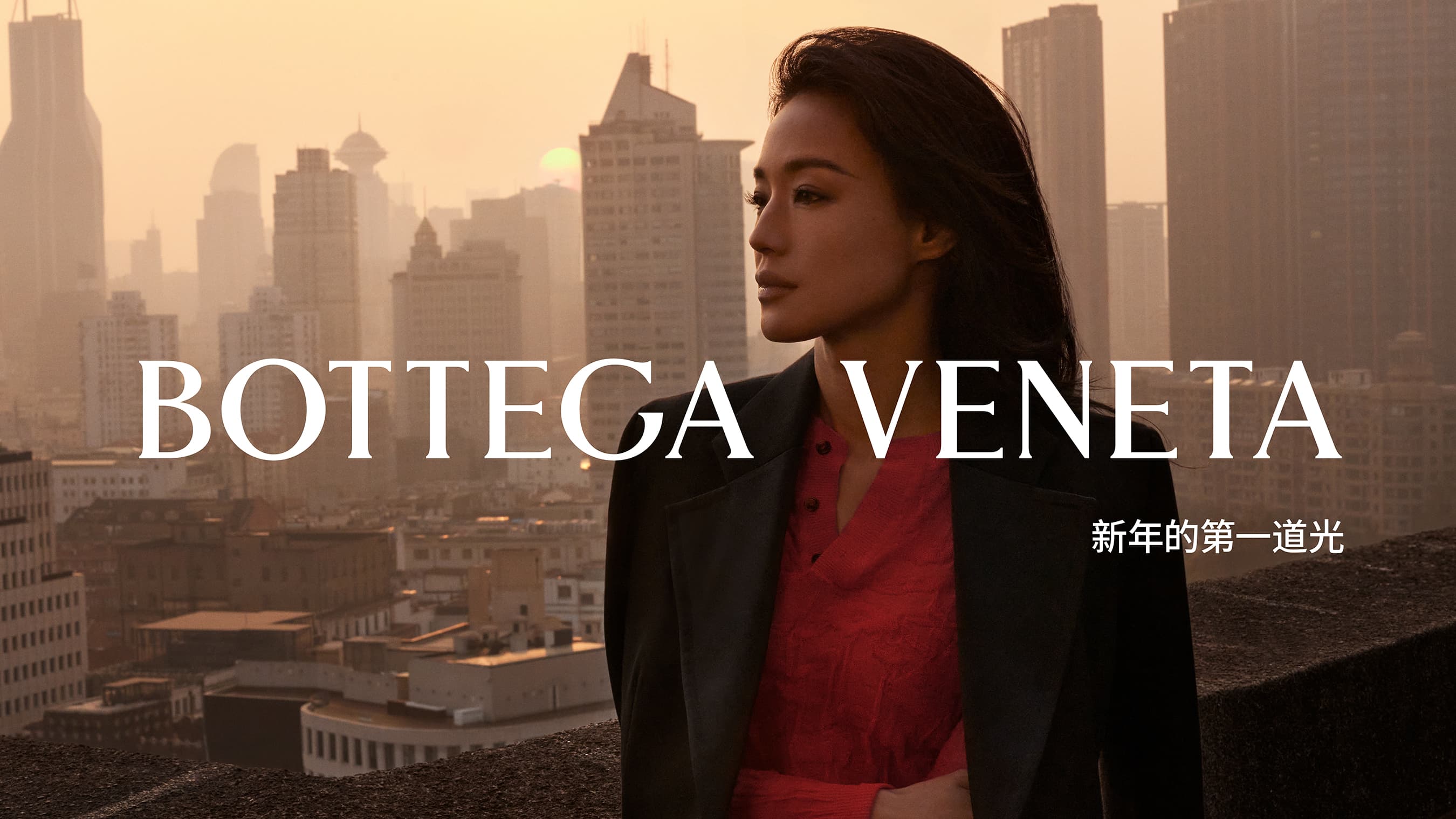 Adult female poses in a fashion shot wearing a blazer with an urban cityscape background and Bottega Veneta branding.