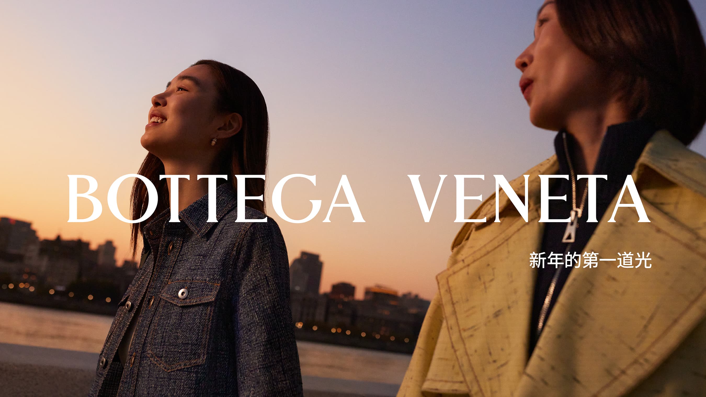 Two adult Asian women pose in Bottega Veneta clothing at sunset with city skyline in the background in a fashion editorial photography.