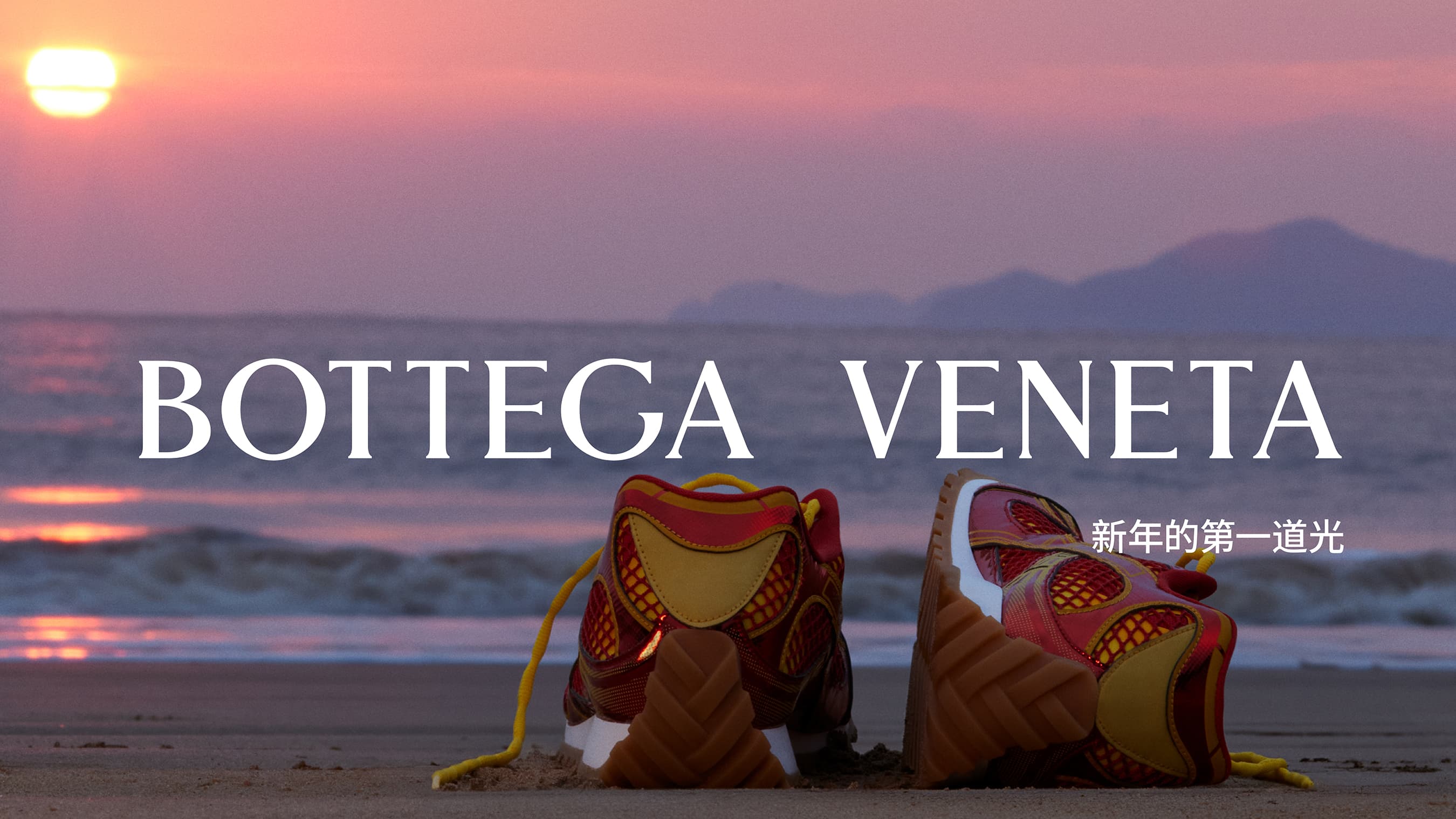 Two Bottega Veneta sneakers are displayed on a sandy beach at sunrise, with a pink and purple sky and gentle waves in the background.