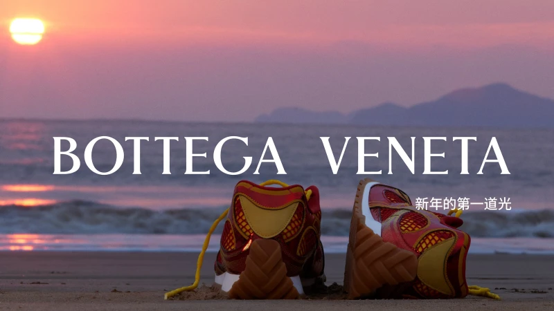Two Bottega Veneta sneakers are displayed on a sandy beach at sunrise, with a pink and purple sky and gentle waves in the background.