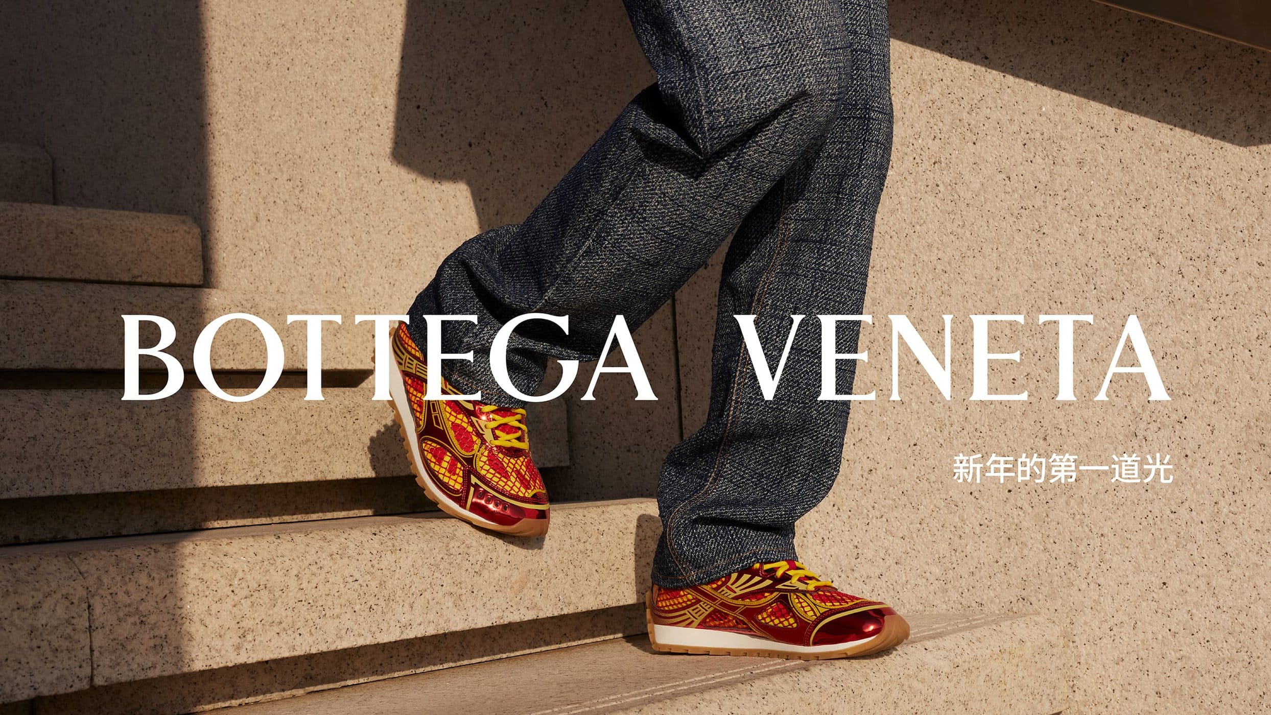 Bottega Veneta sneakers are on display, worn with dark blue denim pants, photographed on stone steps in a brightly lit setting.