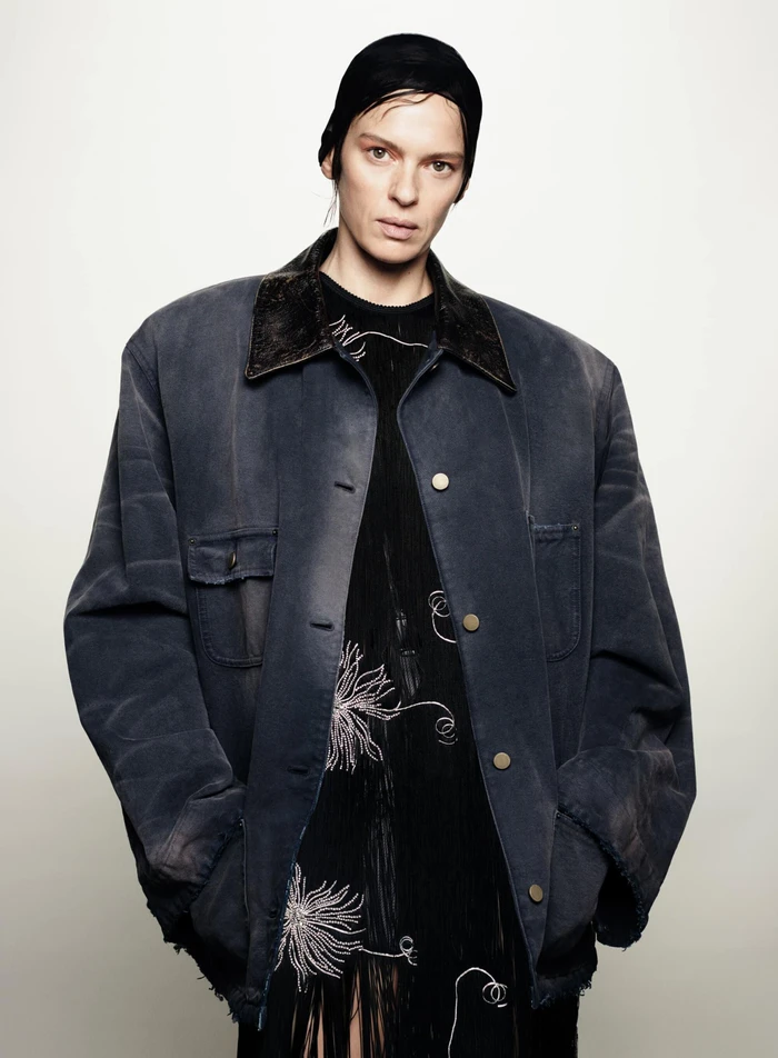 Model wearing a dark oversized jacket and cap against a plain white background for the Prada ad campaign