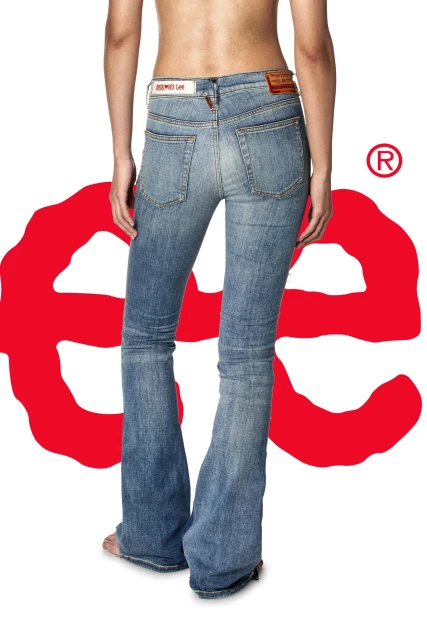 Back view of a woman wearing blue denim jeans with a red logo on a white background. The jeans have a slight bootcut flare.