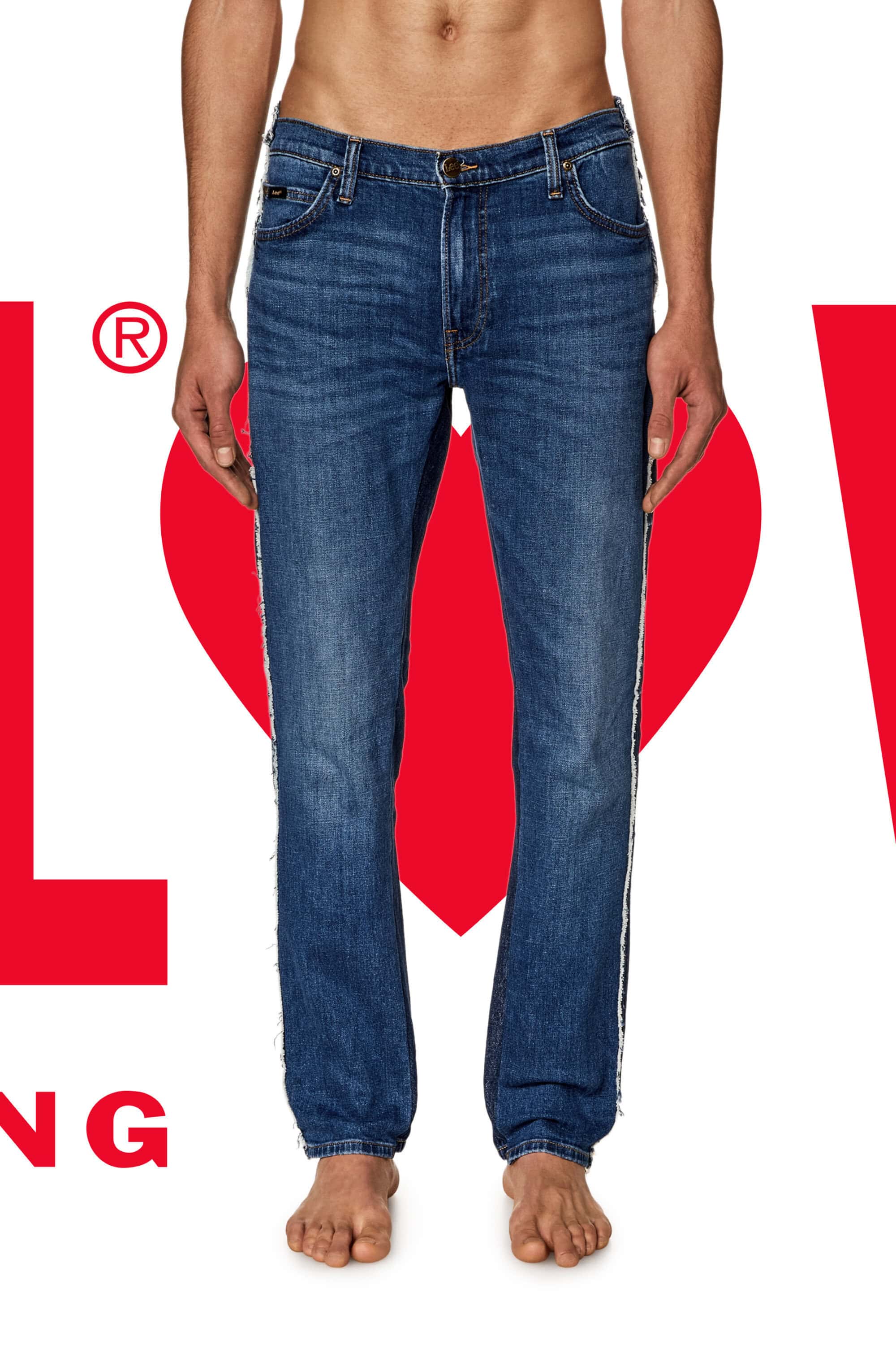 Torso shot of a person wearing denim jeans, standing against a backdrop featuring the logo and the word LOVE, with bare feet.