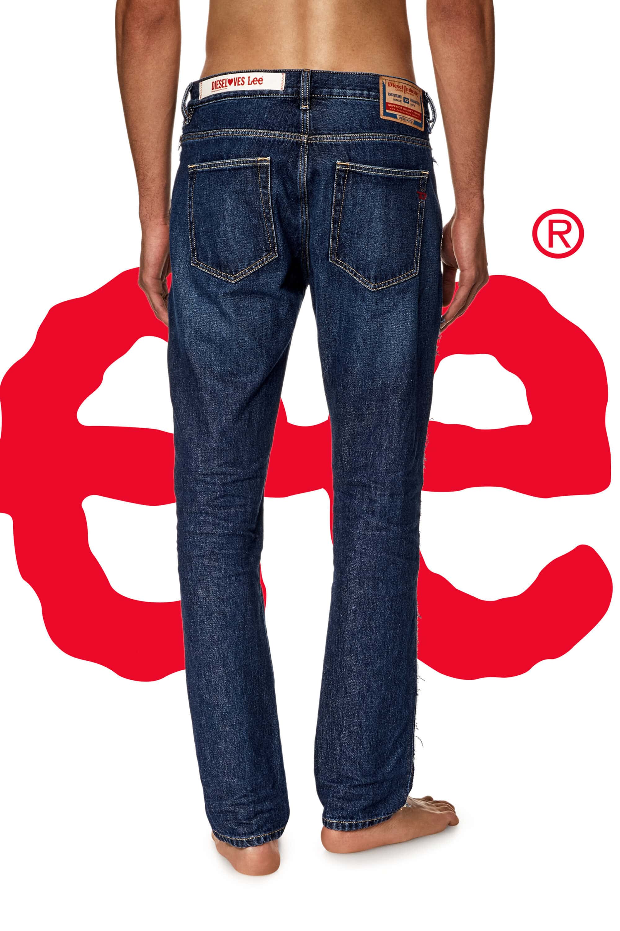 Back view of a person wearing dark blue jeans, standing barefoot against a white backdrop with a large red abstract design.