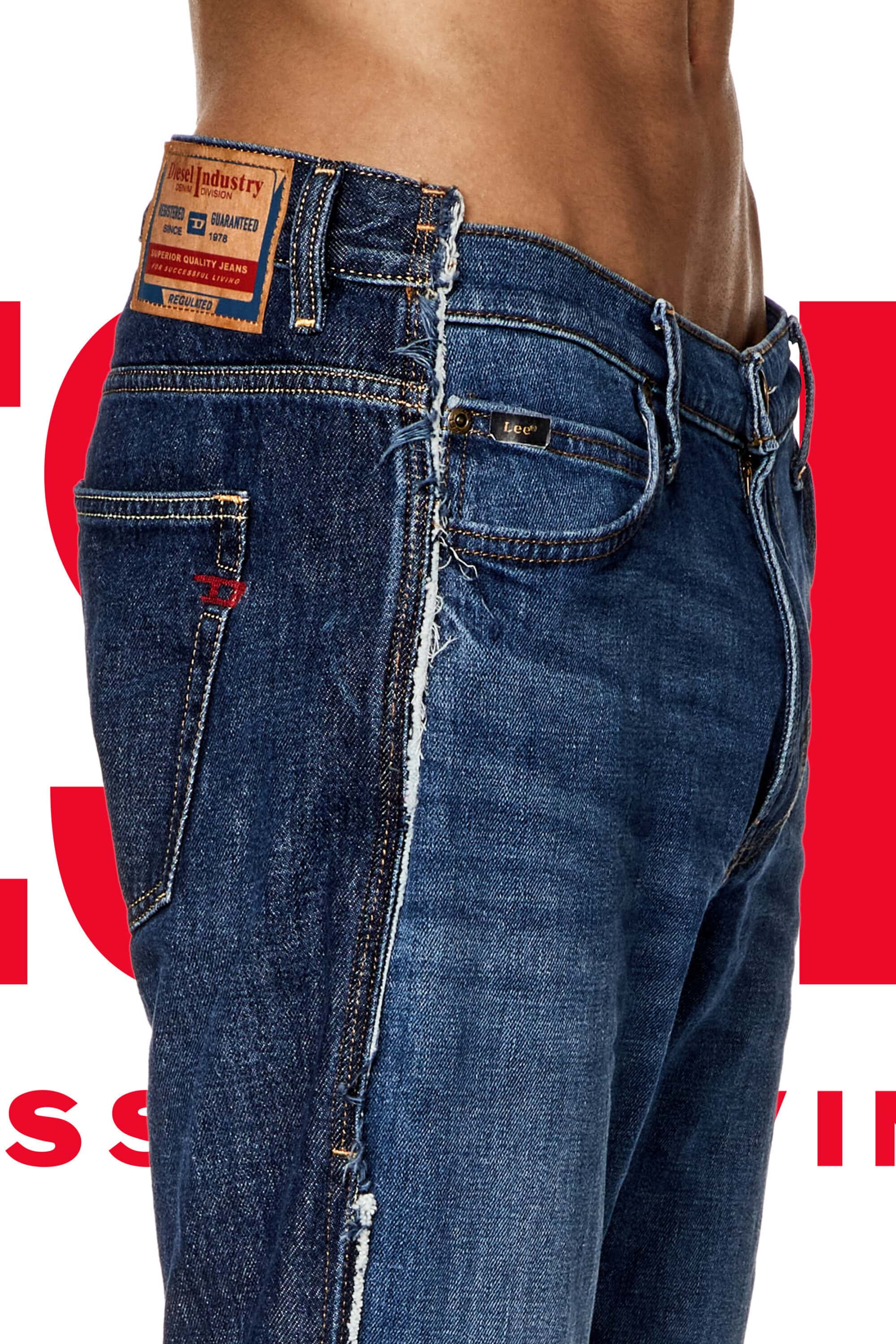 Fashion shot of a man's torso and legs wearing blue denim jeans with ripped details against a red and white studio background.