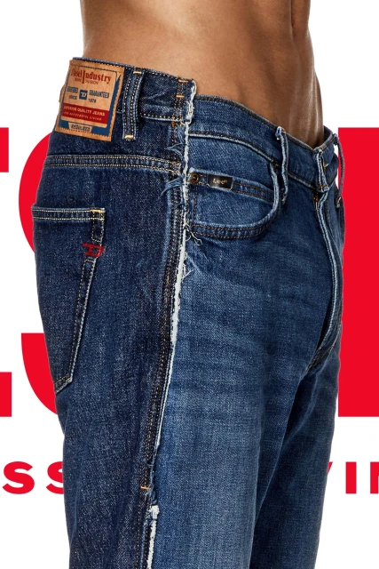 Fashion shot of a man's torso and legs wearing blue denim jeans with ripped details against a red and white studio background.