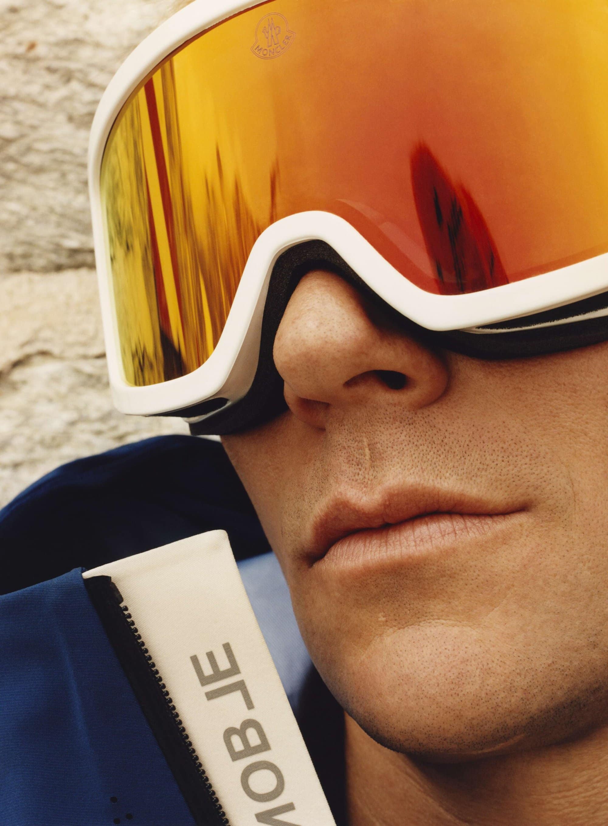 Close-up of a man wearing reflective orange ski goggles and a blue jacket, highlighting winter sports fashion and protective eyewear.