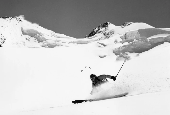 Moncler winter campaign image featuring a skier carving down a steep snowfield beneath snowy mountain peaks.