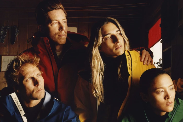 Four individuals wearing colorful winter jackets in a dim wooden interior for the Moncler Winter 2023 ad campaign by Jamie Hawkesworth